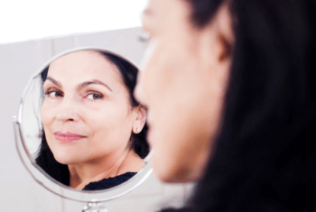 a brunette mature lady smiling in the mirror after a non-surgical facelift